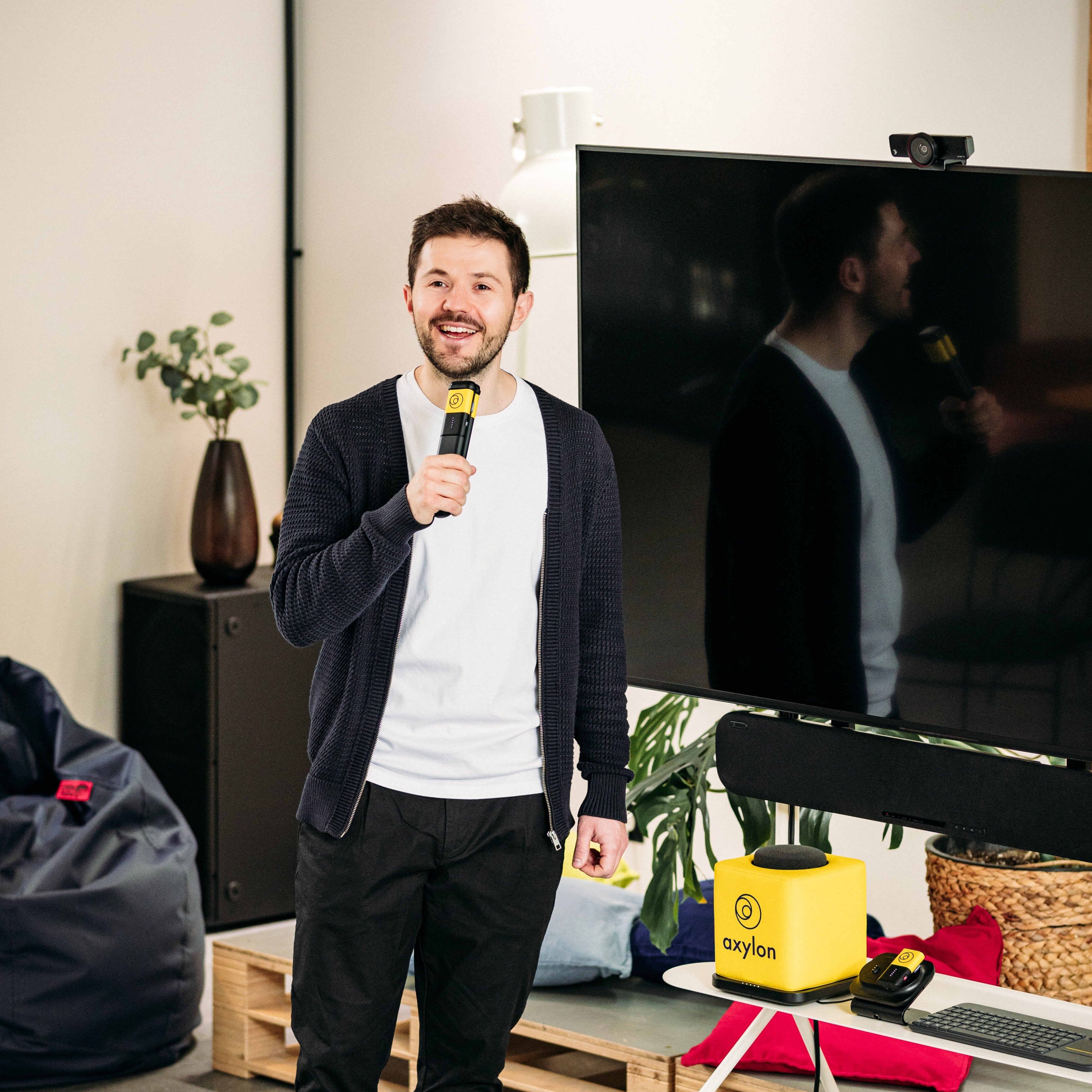 Catchbox Plus used in hybrid meeting room, person holding Stick handheld microphone, placed on the chargers in background are Cube throwable and Clip lavalier microphones